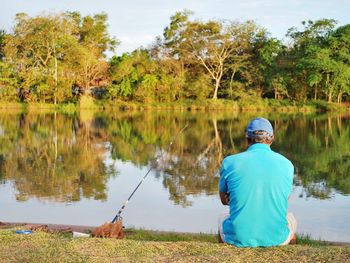 Rear view of man sitting on lake against sky