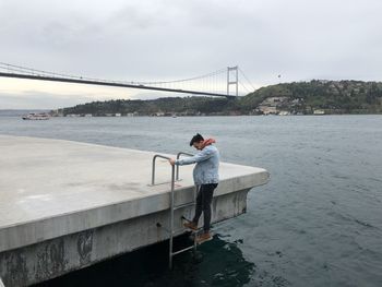 Man standing on bridge over sea against sky