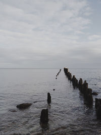 Wooden posts in sea against cloudy sky