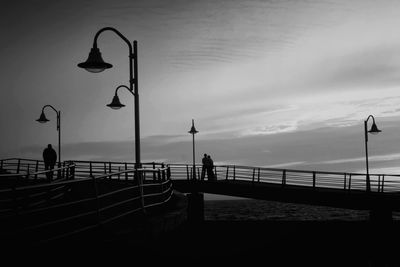 Silhouette people on pier by sea against sky