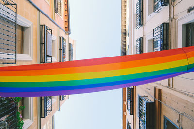 Directly below shot of rainbow flag amidst buildings against sky
