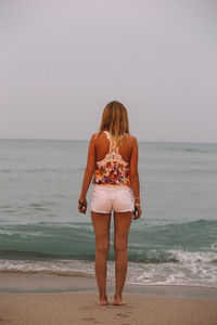 Rear view of woman standing on beach against clear sky