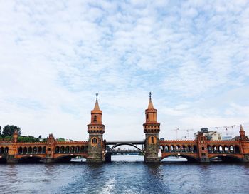 Bridge over river in city against cloudy sky