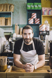 Portrait of confident male retail clerk leaning on checkout counter at grocery store