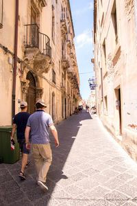 Rear view of people walking on street amidst buildings in city