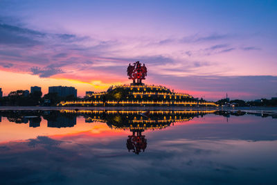 Reflection of buildings in lake against sky during sunset