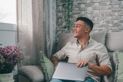 Young man using laptop while sitting on sofa at home