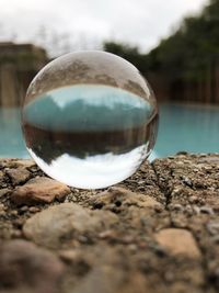Close-up of crystal ball on rock by lake against sky