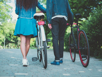 Low section of couple with bicycles walking on footpath at park