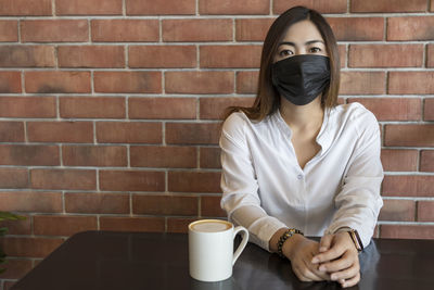 Woman holding coffee cup against wall