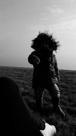 Rear view of child standing on field against sky