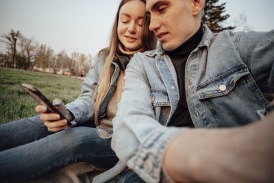 A young fashionable couple smiles while looking at the phone in the park