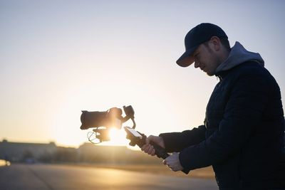 Side view of young man using smart phone against sky