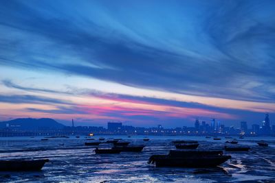 Boats moored at beach against cloudy sky during sunset