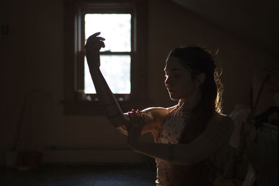 Side view of woman looking through window at home