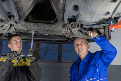 Senior experienced mechanic teaches his colleague how to repair a car