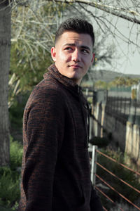 Side view of thoughtful young man standing against trees