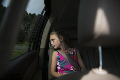 Young blonde girl looks out back window of suv, window light