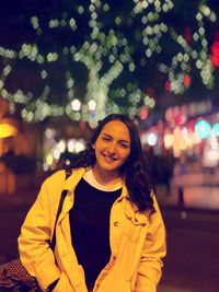 Portrait of smiling young woman standing in illuminated city at night