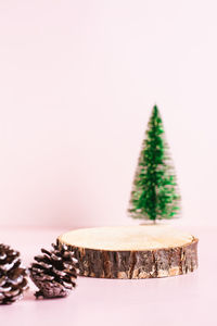 Wood cut podium, decorative christmas tree and pine cones on a pink background vertical view