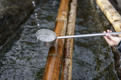 Cropped hand holding ladle over bamboo and water