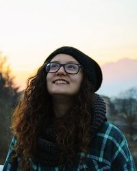Smiling young woman in warm clothes against sky during sunset