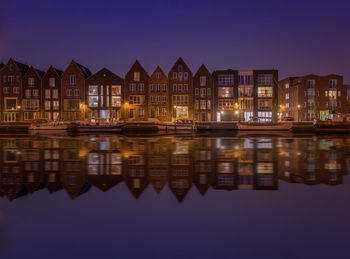 Buildings reflecting on lake in city at dusk