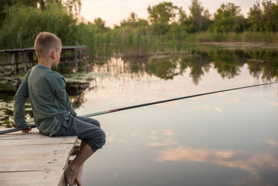 Boy on pier fishing in lake against sky