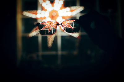 Close-up of hand holding eyeglasses against illuminated christmas lighting equipment