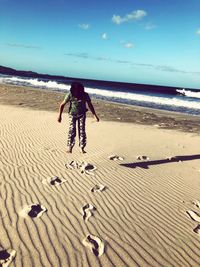 Rear view of woman on beach against sky
