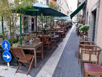 Empty chairs and tables at sidewalk cafe amidst buildings in city