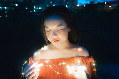 Portrait of beautiful woman holding illuminated light at night