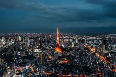 Aerial view of illuminated tokyo tower amidst buildings against cloudy sky in city at night