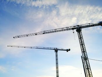 Low angle view of silhouette cranes against sky