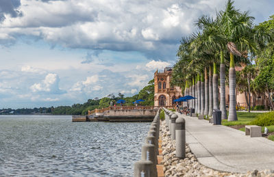 Bridge over river by palm trees and buildings against sky