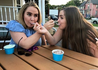 Woman feeding ice cream to each other while sitting on table