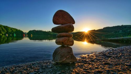 Stack of rocks by lake against sky during sunset