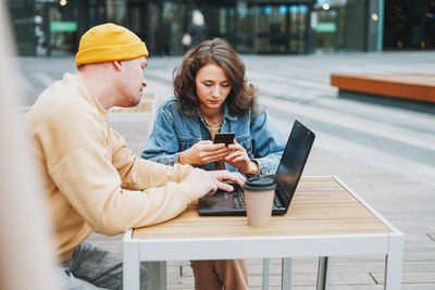 Stylish young couple freelancers working on laptop in street cafe