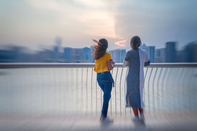 Woman standing on railing against sky in city