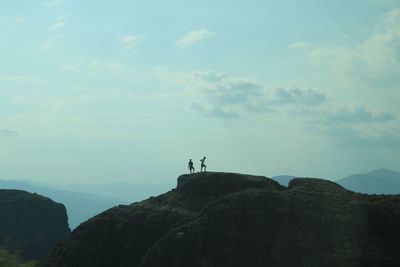 People standing on rock by mountain against sky