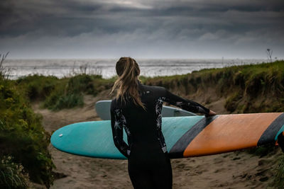 Rear view of woman with surfboard on beach against sky