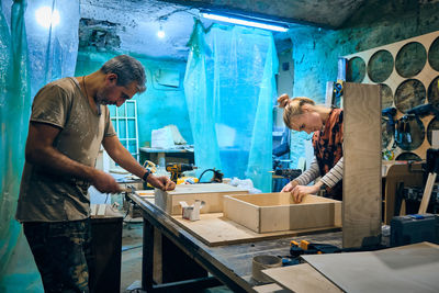 Caucasian grey-haired man and young adult woman assembling furniture. working progress at workshop.
