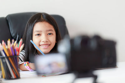 Portrait of smiling girl holding camera on table