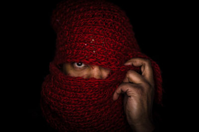 Close-up portrait of man covering face with scarf against black background