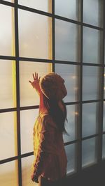 Side view of girl touching glass while standing by window