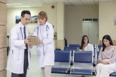 Doctors from asia and the west hold a tablet and converse about a patient at a hospital.