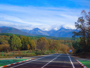 Road amidst trees and mountains against sky