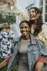 Happy mature woman piggybacking daughter at social gathering with family in back yard