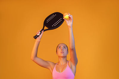 Woman playing tennis against orange background