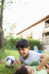 Playful boy lying at lawn against sky